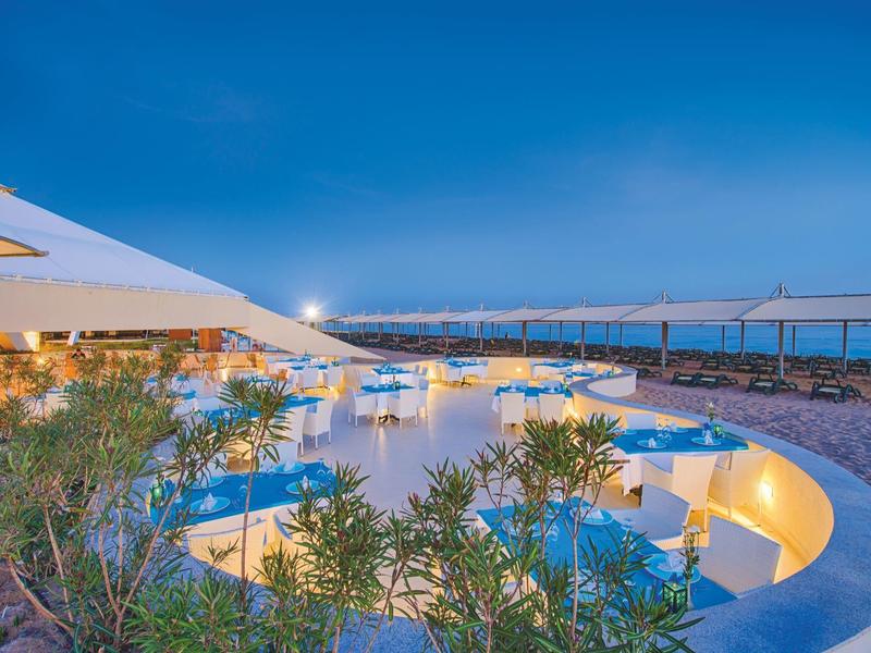 Zakřivená oblast bazénu s modrou vodou a rostlinami pod jasnou večerní oblohou.