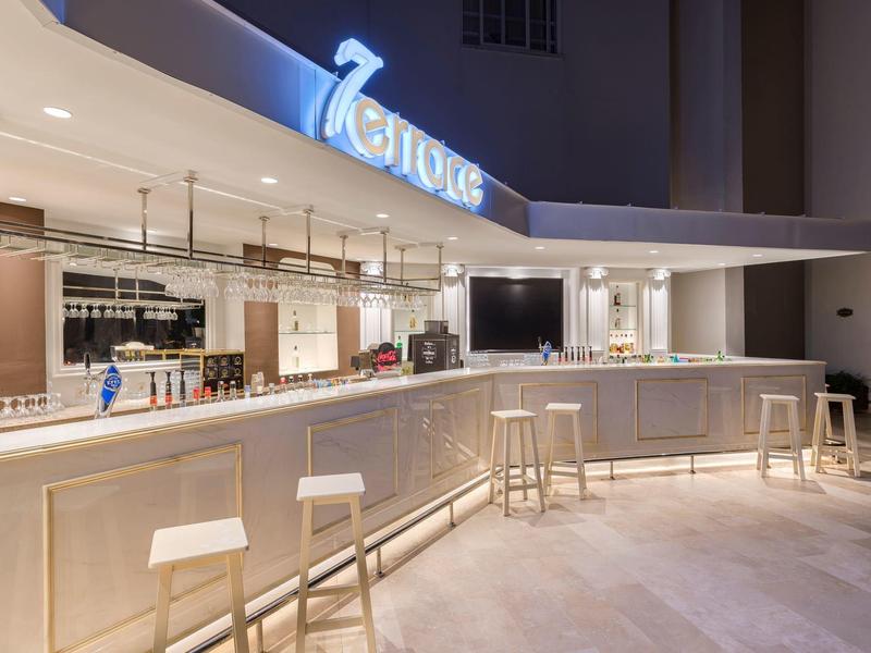 Moderní venkovní bar se stoličkami a osvětleným nápisem "7 Oceans" v noci.