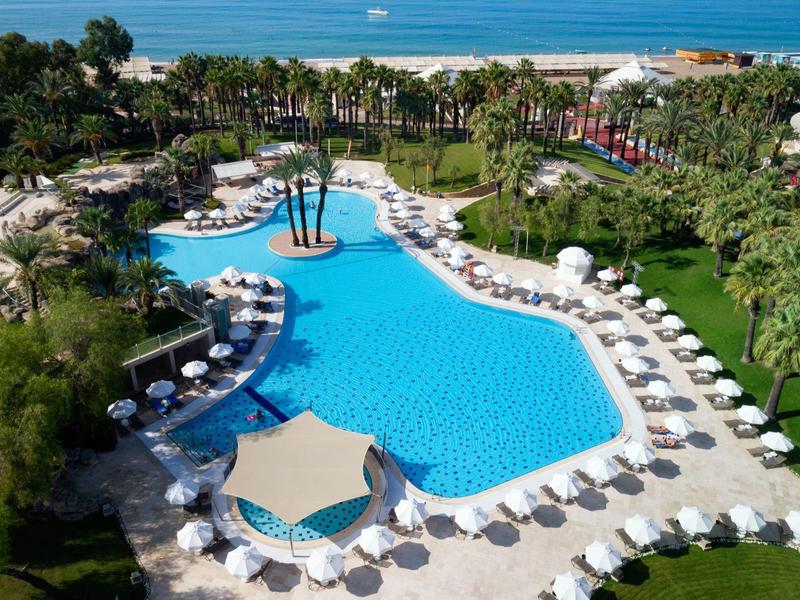 Velký venkovní bazén s lehátky a slunečníky poblíž pláže s palmami.