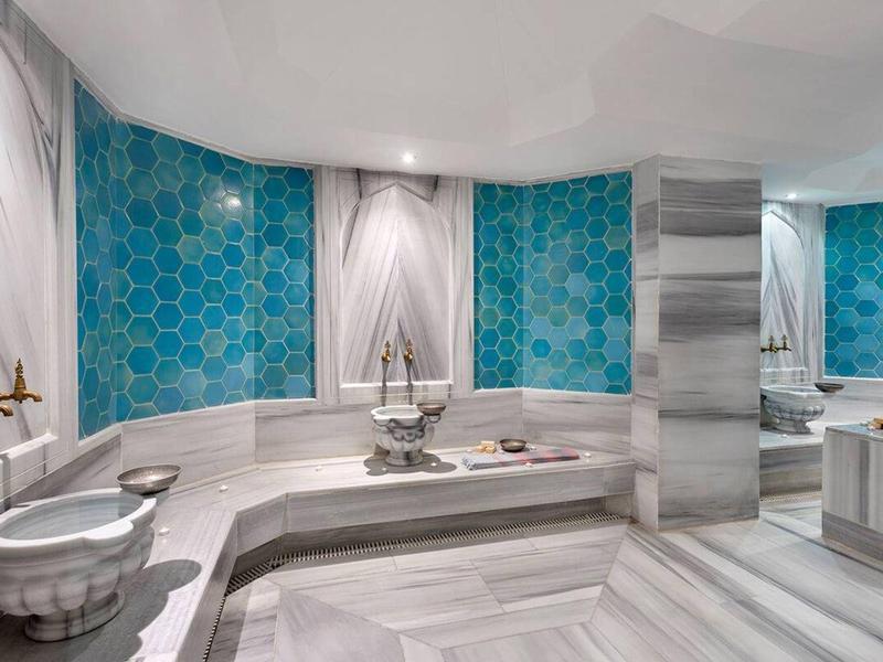 Prostorná lázeňská místnost s velkou mramorovou vanou, modrými obklady a elegantními prvky.