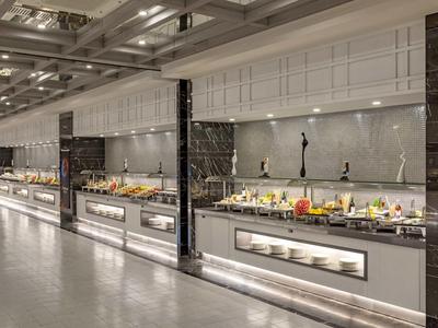 Moderna recepción de hotel con buffet largo y diversas comidas bajo luz brillante.