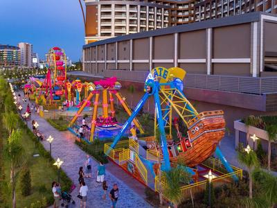 Parque de atracciones colorido con varias atracciones junto a un gran hotel al anochecer.