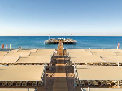Large jetée mène à une plateforme au-dessus de la mer calme sous un ciel ensoleillé, plages de chaque côté.