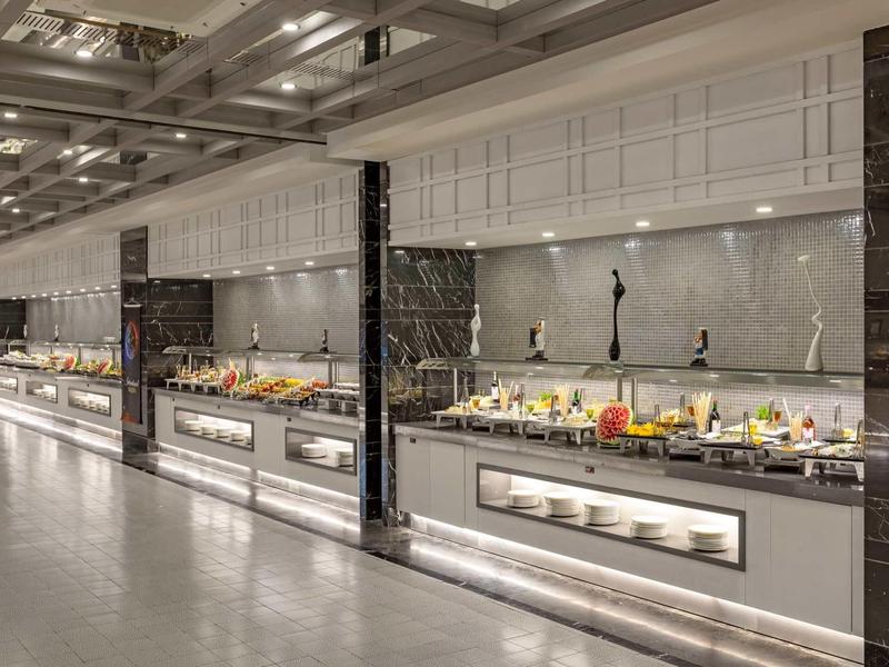 Moderna recepción de hotel con buffet largo y diversas comidas bajo luz brillante.