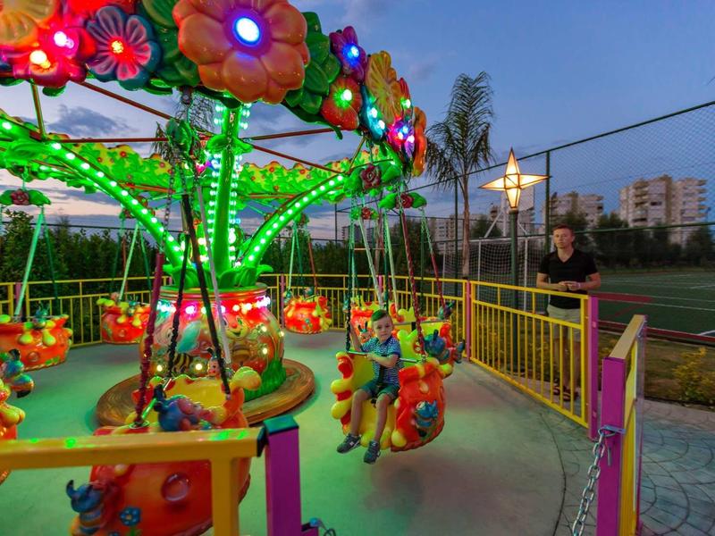 Carrusel columpio infantil colorido y iluminado en un área exterior al atardecer.