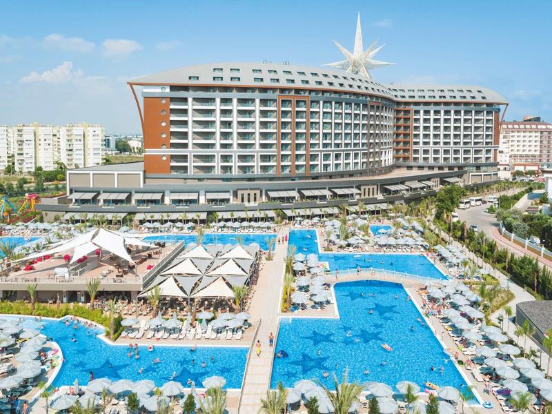 Gran hotel con varias piscinas y terrazas soleadas bajo un cielo azul.