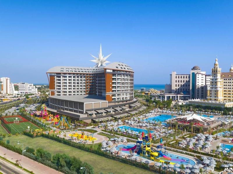 Gran hotel de lujo con zona de piscinas y toboganes acuáticos cerca del mar bajo cielo despejado.