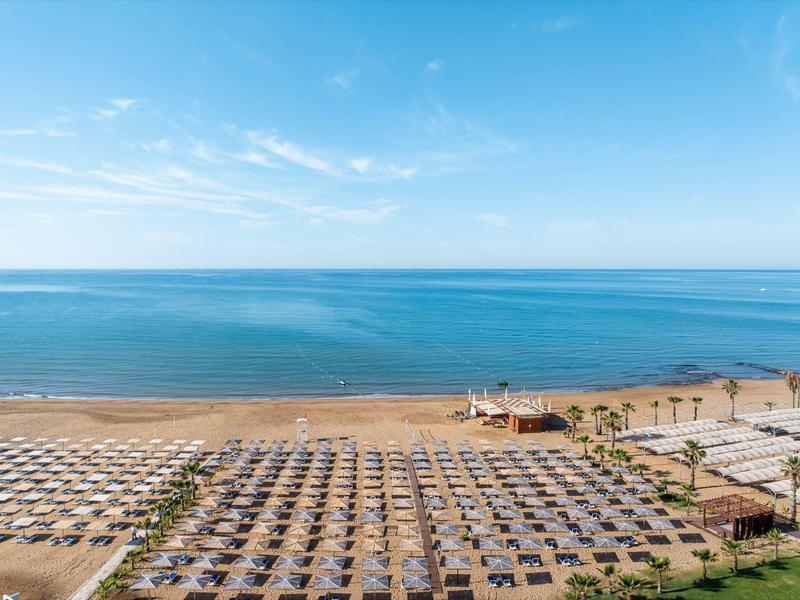 Amplia playa con filas de sombrillas y mar azul claro al fondo.