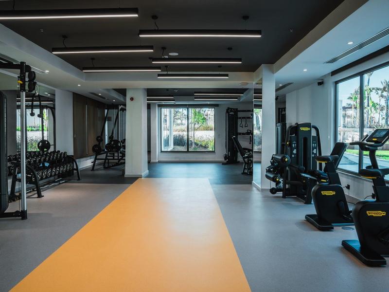 Gimnasio moderno con equipos de entrenamiento y grandes ventanales con vista exterior.