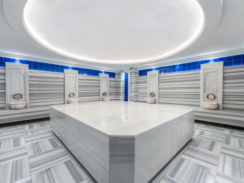 Amplia sala de spa moderna con mesa central de piedra calefaccionada y luz redonda en el techo.