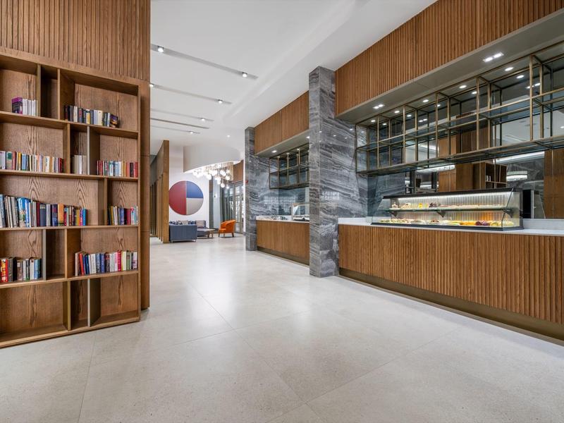Área moderna del hotel con biblioteca, estanterías de madera y mostrador de recepción de madera y vidrio.