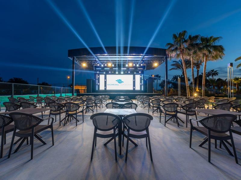 Área de cine al aire libre de un hotel con filas de asientos y pantalla iluminada por la noche.