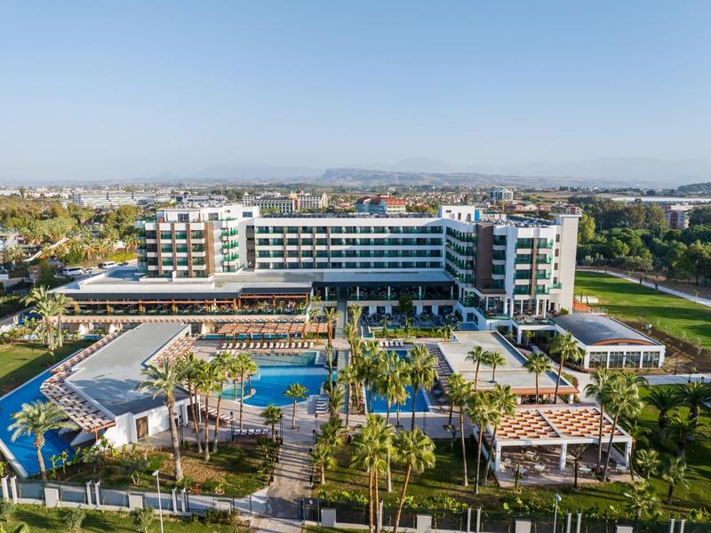Gran hotel con piscinas, palmeras y jardines bajo un cielo despejado.