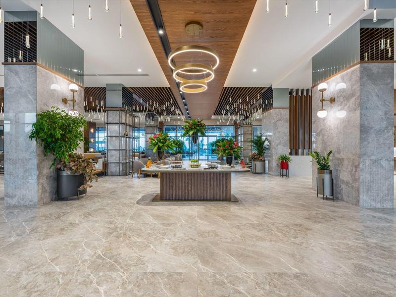 Área de vestíbulo de hotel moderno con suelo de mármol, plantas y luces colgantes.