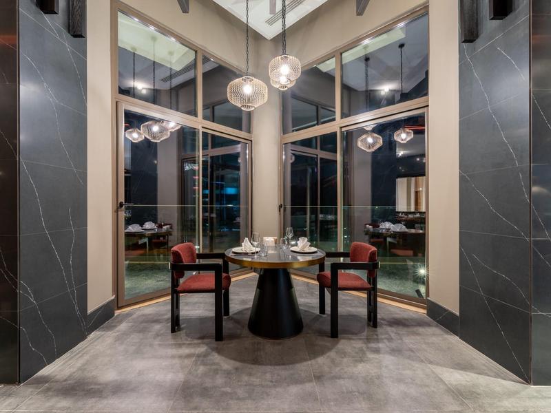 Área de comedor elegante con mesa redonda y dos sillas junto a grandes ventanas y lámparas colgantes