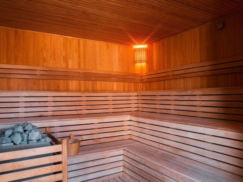 Sauna de madera con bancos en forma de U, horno de sauna con piedras y un cubo de madera.