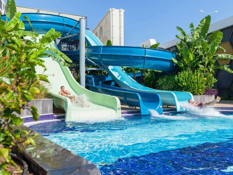 Several water slides empty into a pool surrounded by lush vegetation.