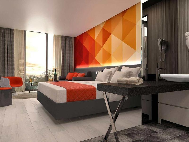 Modern hotel room with large bed, geometric wall design, and panoramic window.