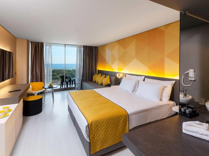 Modern hotel room with double bed, yellow bedspread, balcony, and open view of the landscape.