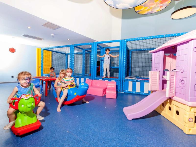 Children playing in a bright indoor play area with slide and soft toys.