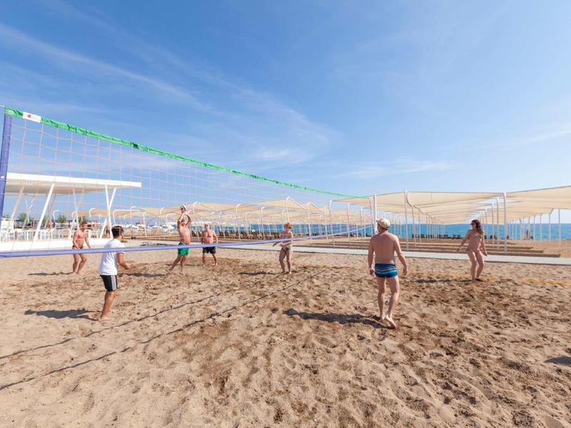 People playing volleyball on a sunny beach with blue sky and sunshade.