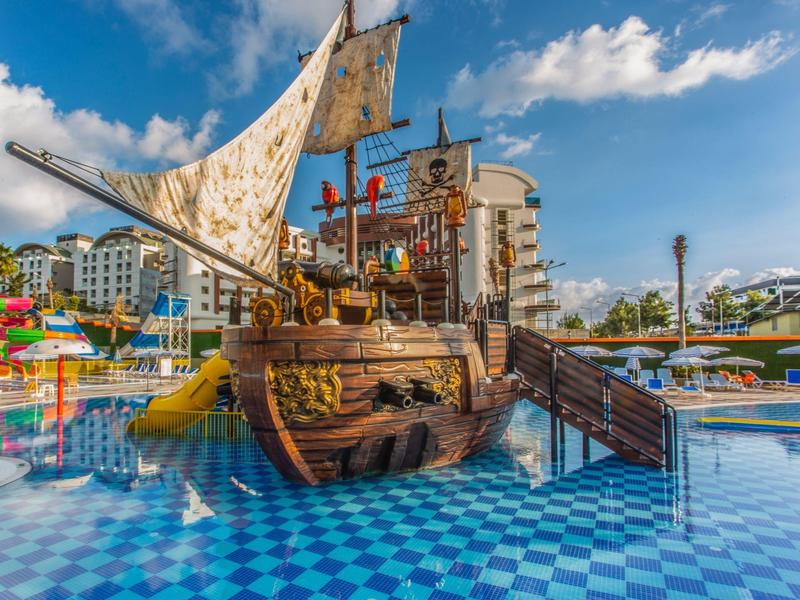 Children's playground with pirate ship and slides in a sunny pool area