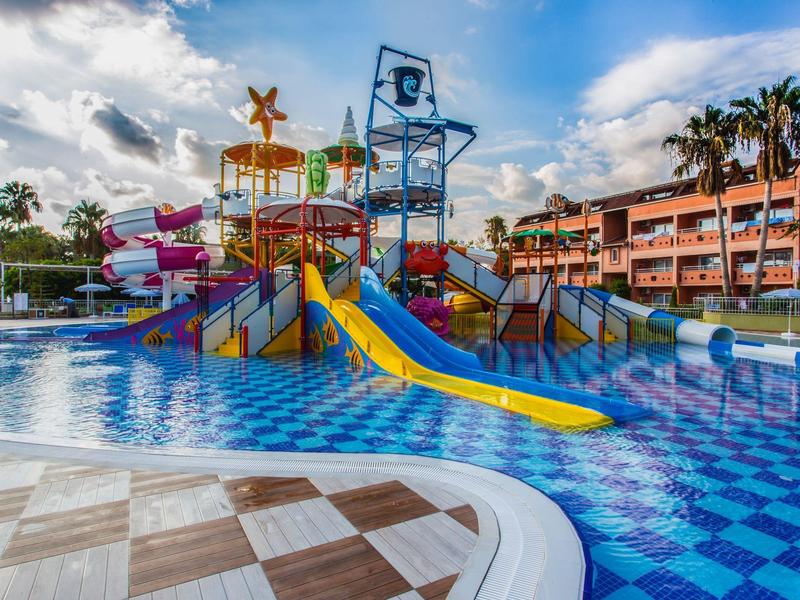 Colorful water park with slides and splash pool next to hotel buildings under a blue sky.