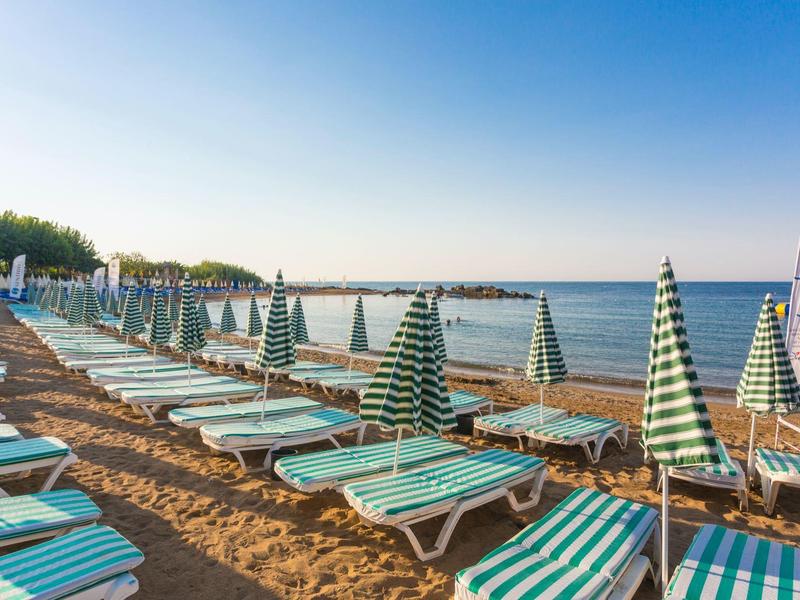 Beach with rows of lounge chairs and closed green and white striped umbrellas by the sea