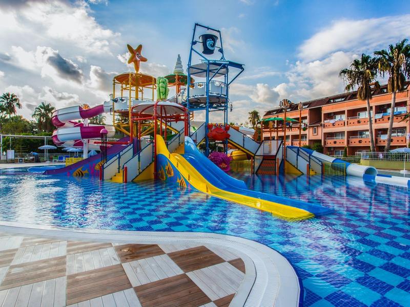 Colorful water park with slides, splash pools, and hotel building in the background under sunny sky