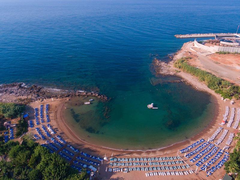 Semi-circular beach with blue and white striped sun loungers overlooking clear blue sea.