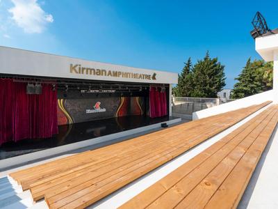 Open-air stage with wooden benches and red curtain under clear sky.