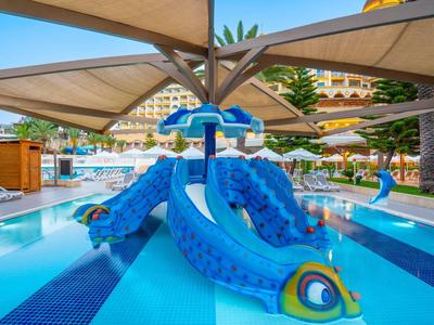 Kleurrijke kinderspeelplek met glijbaan in een hotelzwembad onder parasols.