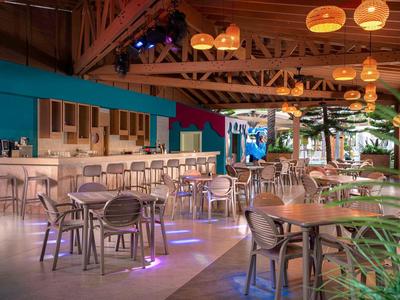 Moderne hotelbar met houten tafels, stoelen en warme plafondlampen.