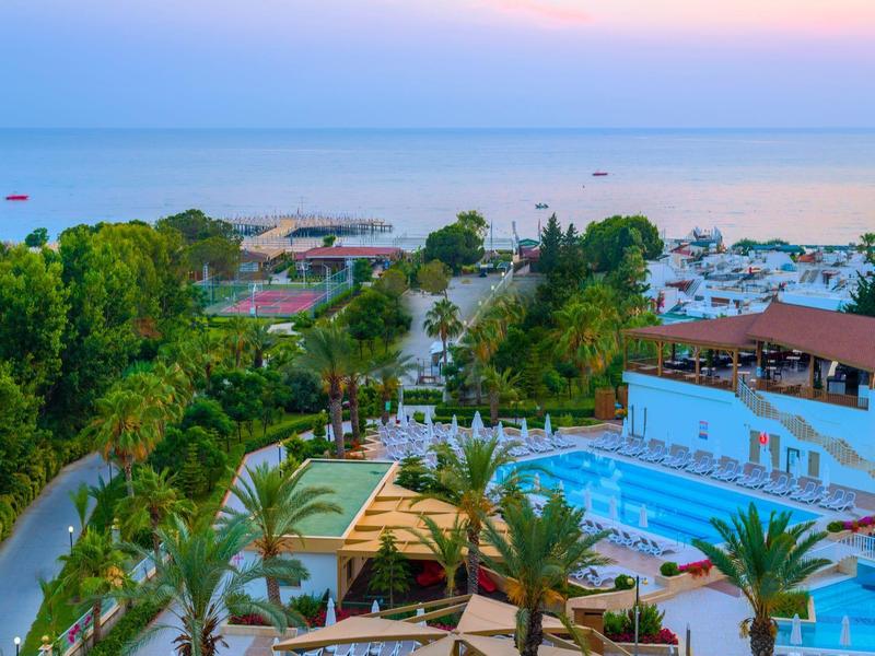Uitzicht op een hotelzwembad met palmbomen en zeezicht bij zonsondergang