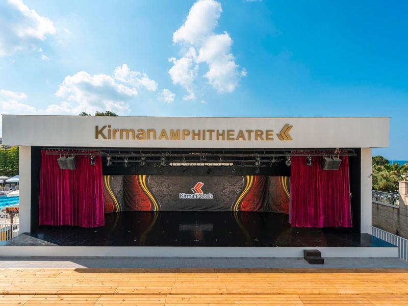 Open amfitheaterpodium met rode gordijnen onder een blauwe lucht met witte wolken.