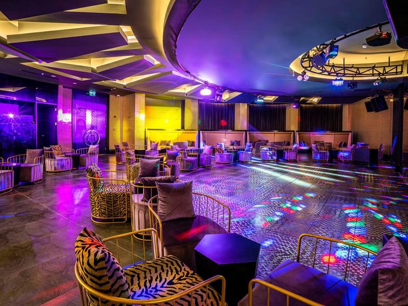 Ruime stijlvolle nachtclub met dansvloer, kleurrijke lichten en gezellige zitgedeeltes.