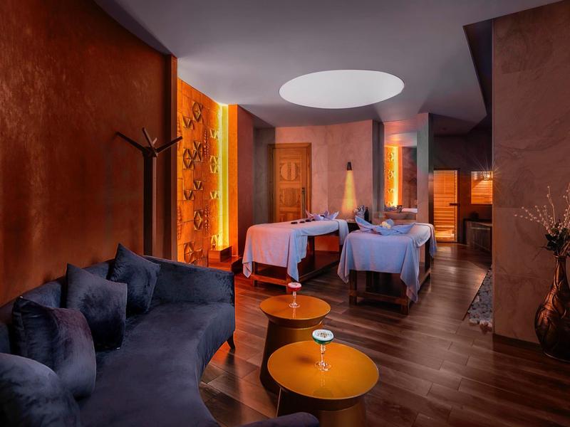 Gezellige behandelruimte met massagetafels, warm licht en donkerblauwe bank in een spa-gebied.