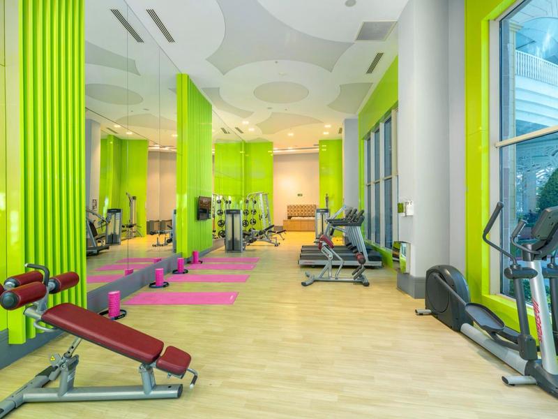 Lichte fitnessruimte met groene muren, halters, trainingsbanken en grote ramen.