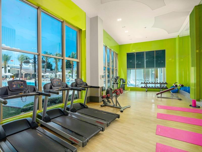 Moderne fitnessruimte met loopbanden, yogamatten en grote ramen met uitzicht op buiten.