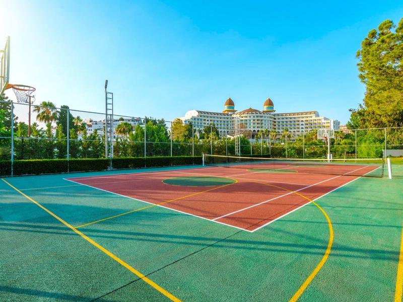 Leeg basketbalveld met hotelgebouw op de achtergrond en een heldere lucht overdag.