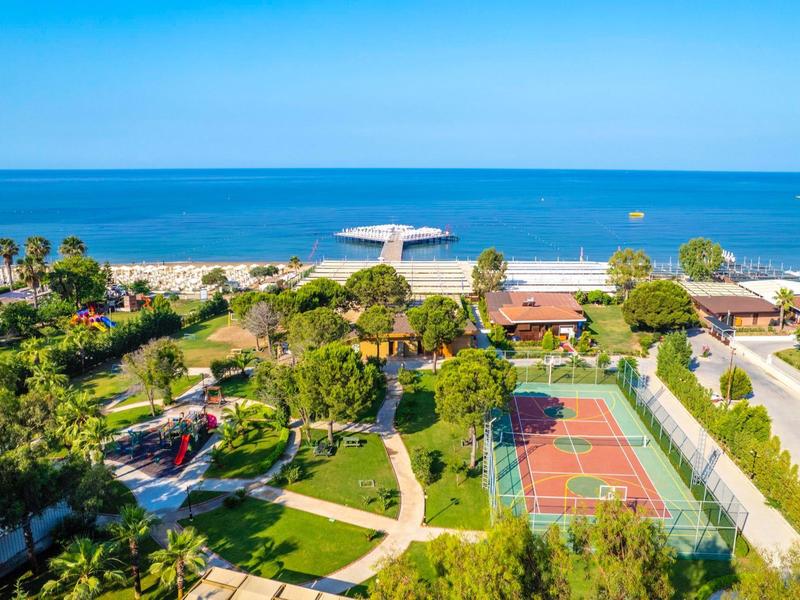 Uitzicht op hotelterrein met tennisbaan, tuin en strand aan zee onder een heldere lucht