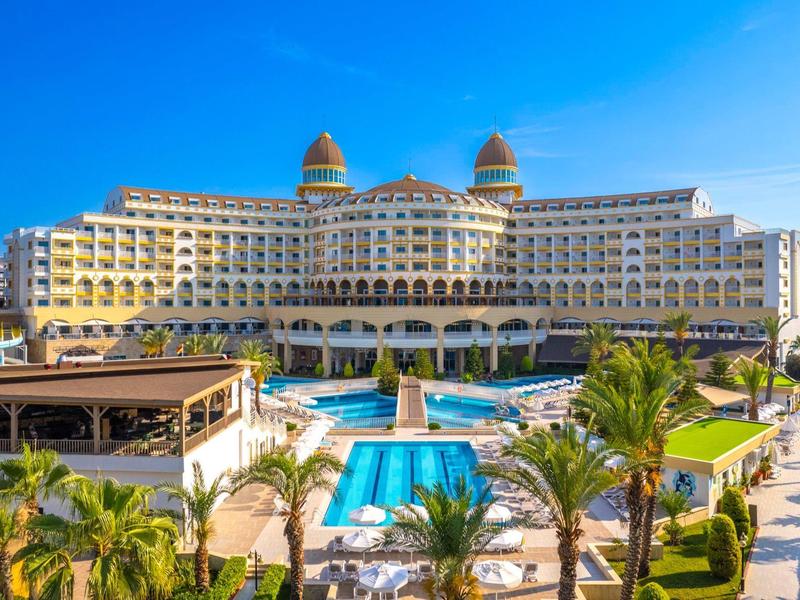 Luxe hotel met meerdere zwembaden, palmbomen en bloeiende tuinen bij zonnig weer.