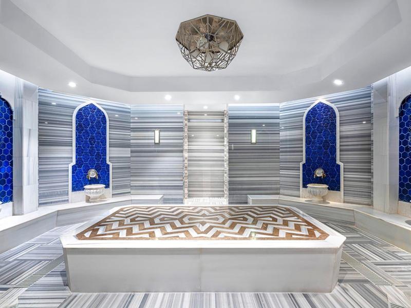Elegant hammam met marmeren bassin en blauwe betegelde nisjes onder een stijlvolle koepel.