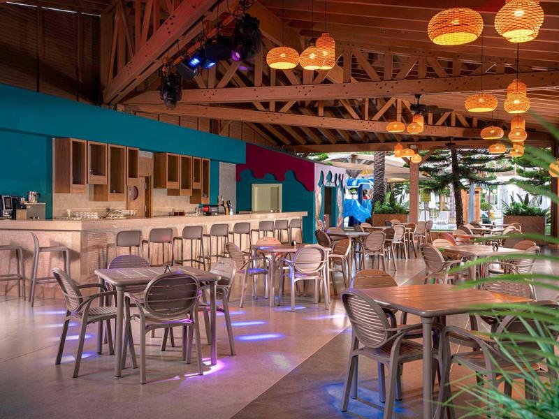 Moderne hotelbar met houten tafels, stoelen en warme plafondlampen.