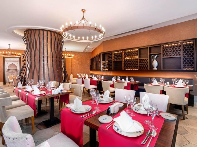 Elegant restaurant met rood gedekte tafels en moderne witte stoelen in een warme sfeer.