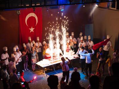 Koks en mensen vieren rond een tafel met sterretjes en Turkse vlag.