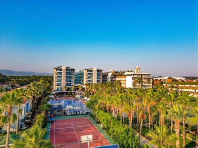 Hotel de lujo con piscina y pista de tenis, rodeado de palmeras y vegetación bajo un cielo azul claro.