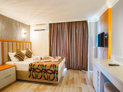 Modern eingerichtetes Hotelzimmer mit Doppelbett, Nachttisch, Kissen und Vorhängen in gedeckten Farben.