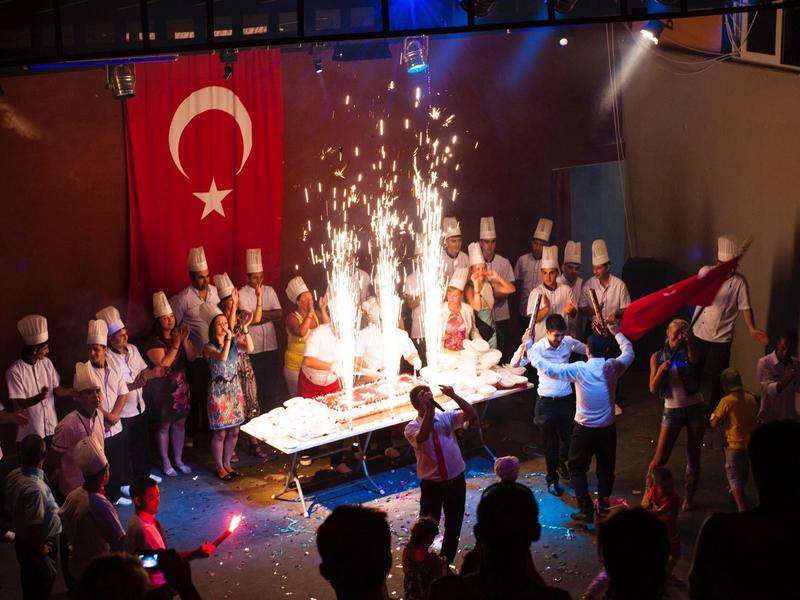 Koks en mensen vieren rond een tafel met sterretjes en Turkse vlag.