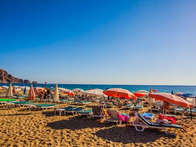 Strand met kleurrijke parasols en ligstoelen onder een blauwe hemel bij de zee.